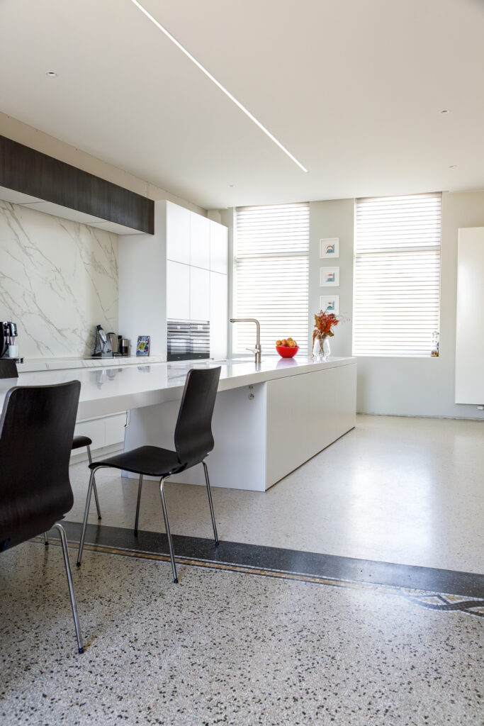 Zicht vanuit de keuken op eetkamer met originele terrazzo en nieuwe terrazzo gietvloer in kunsthars met subtiele messing overgang