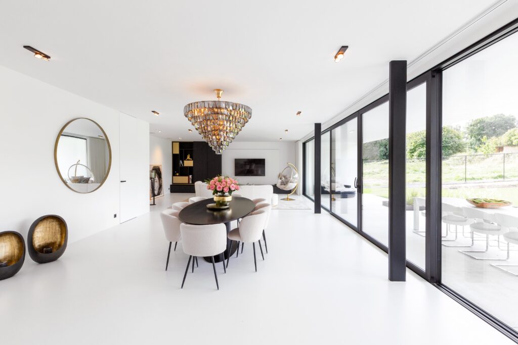 Eetkamer met witte PU Comfort+ gietvloer, grote raampartijen en gouden accenten in een strakke woning in Landen