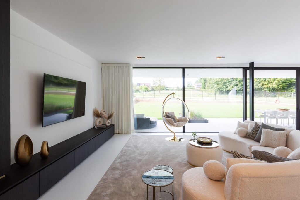 Woonkamer met witte PU Comfort+ gietvloer, Thonon maatmeubel, gouden accenten en uitzicht op de tuin