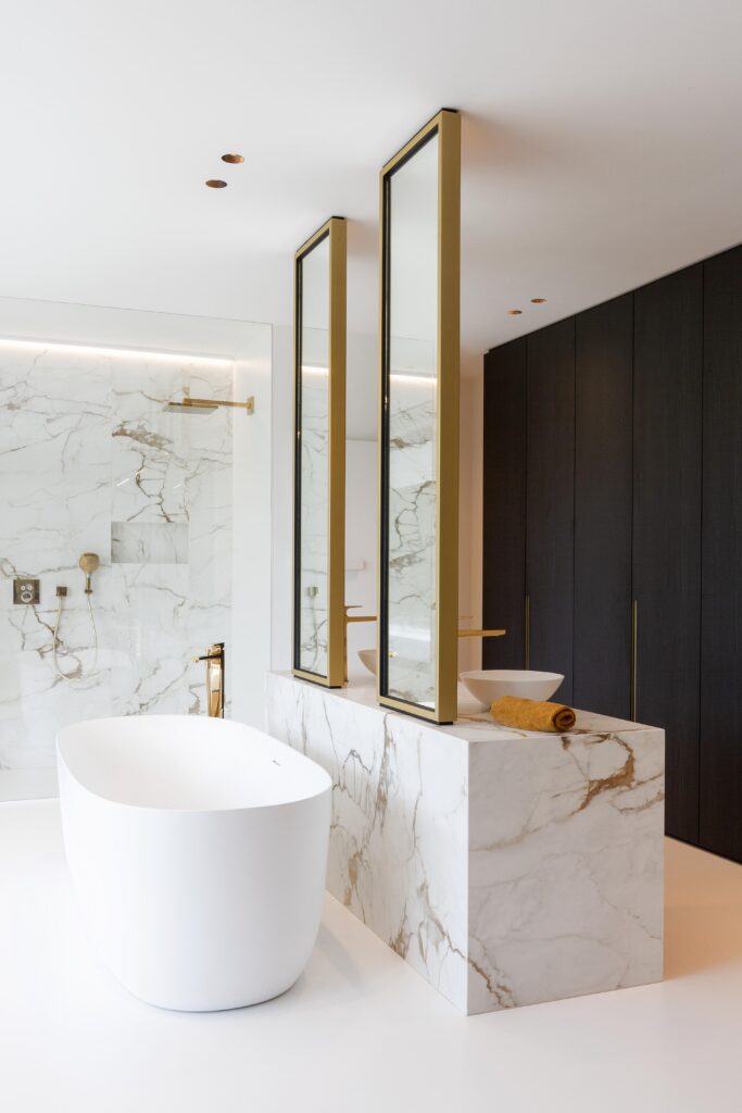 Badkamer met witte PU Comfort+ gietvloer, vrijstaand bad, marmer met gouden aders, gouden kranen en spiegels