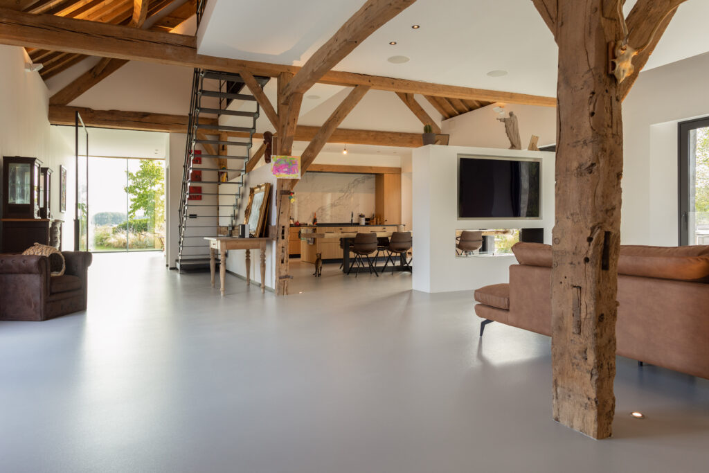 PU gietvloer en houten balken in hoeve-renovatie – Moderne gietvloer contrasteert subtiel met rustieke houten accenten voor een warme uitstraling.
