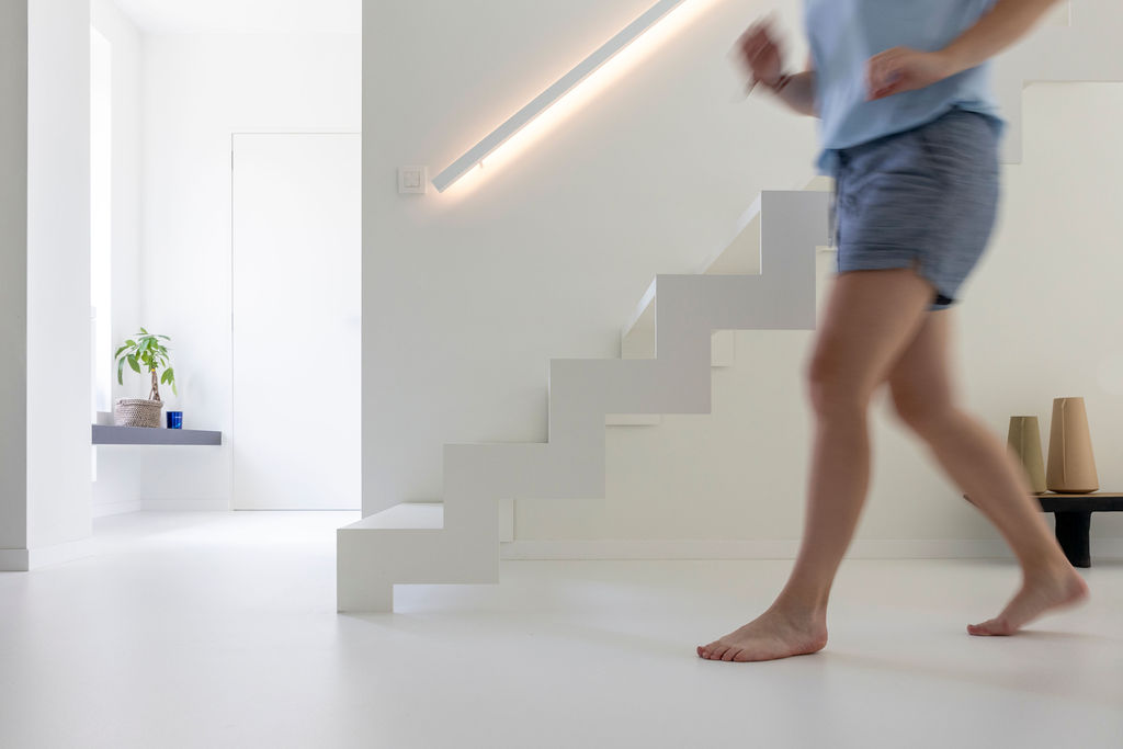 Naadloze witte gietvloer met een elegante witte trap op de achtergrond, in een moderne villa met veel lichtinval.