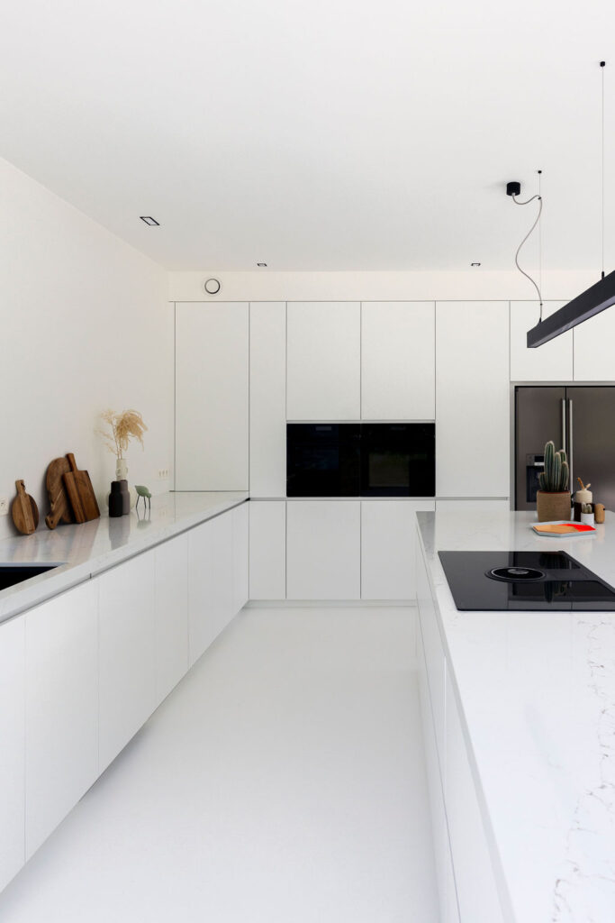 Strakke witte maatkeuken in een moderne villa met naadloze witte gietvloer en veel lichtinval door grote zwarte raampartijen.