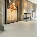 Mineral Touch gietvloer in loft met groot kunstwerk en bureauhoek tegen bakstenen muur.