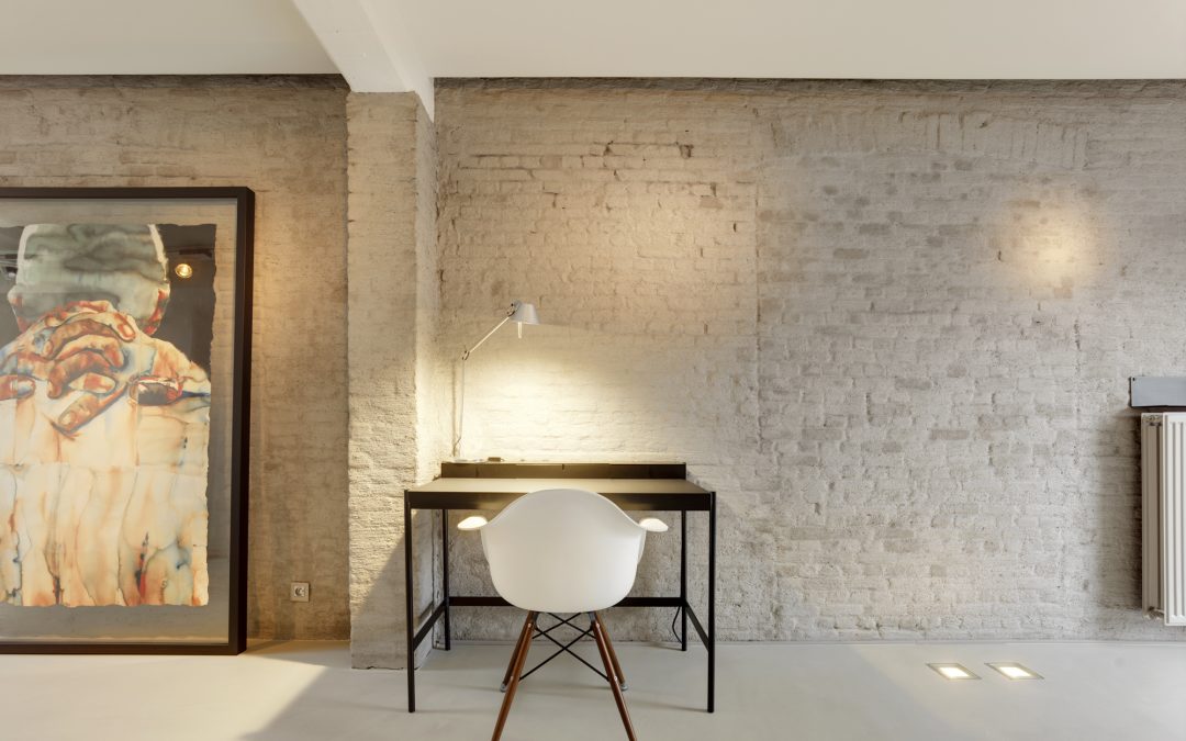 Werkhoek met bureau en designstoel op Mineral Touch gietvloer tegen bakstenen muur.