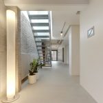 Gang met Mineral Touch gietvloer en planten onder industriële trap in loftwoning.