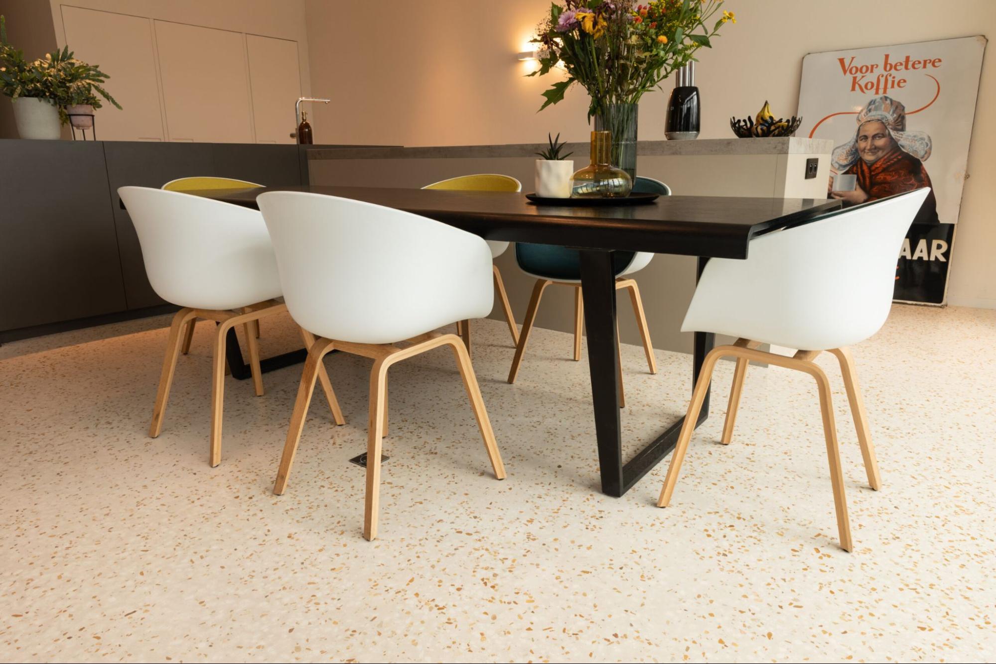 Eetkamer met terrazzo gietvloer in renovatie, moderne stoelen en warme interieuraccenten<br />
