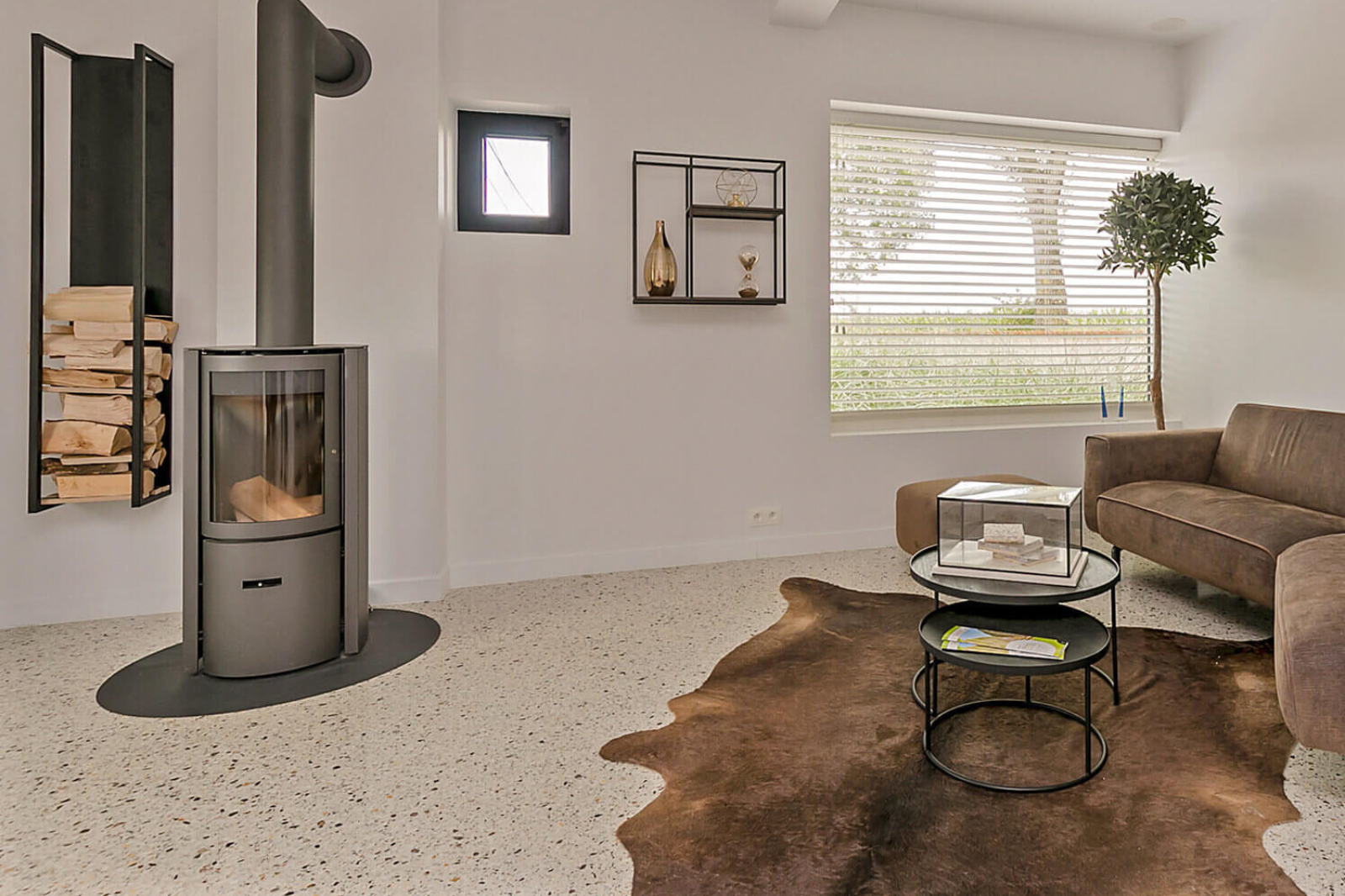 Moderne woonkamer met houtkachel en naadloze terrazzo vloer met lichte steenkorrelstructuur.<br />
