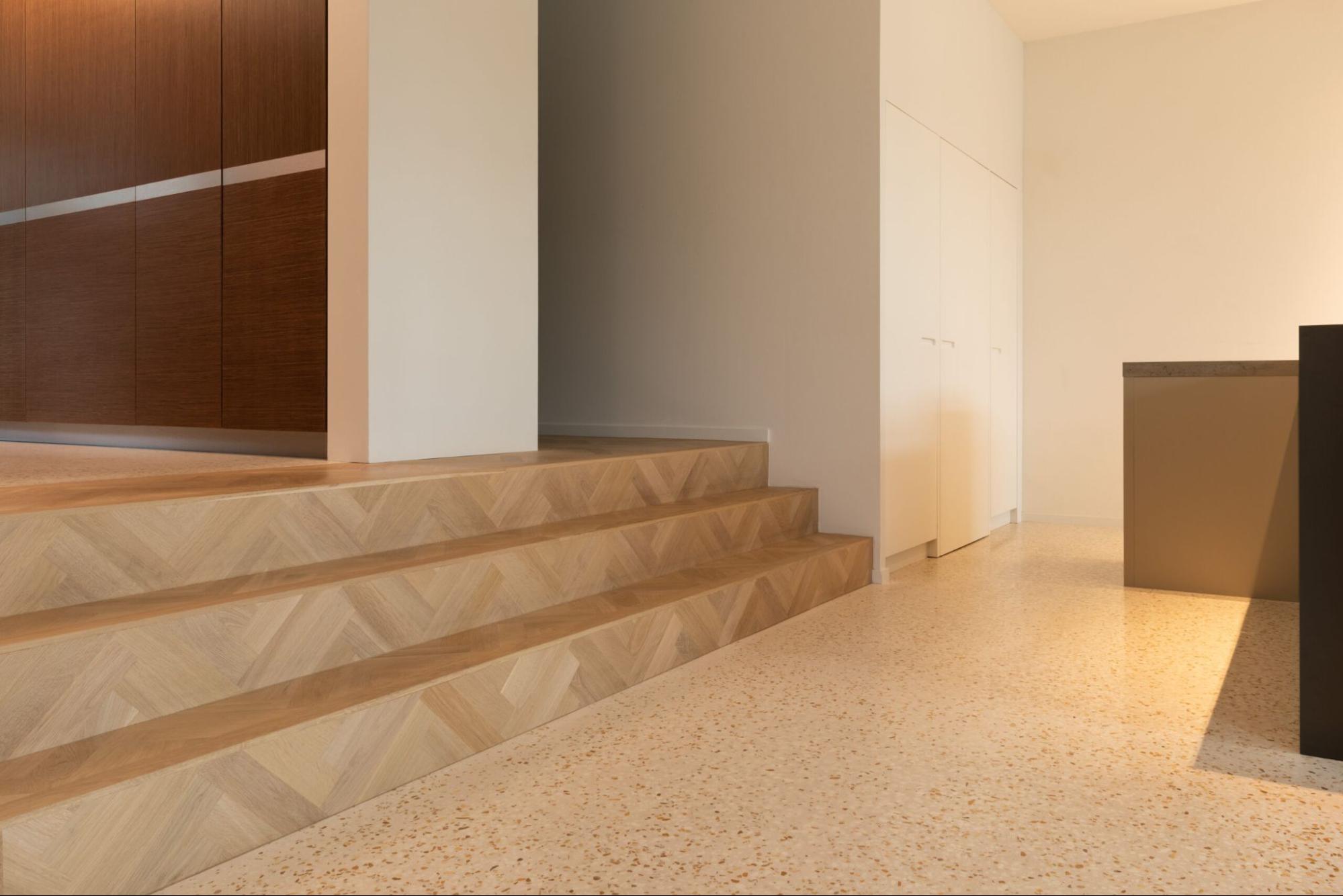 Moderne inkomhal met houten trap en lichte terrazzo vloer met fijne steenkorrel.
