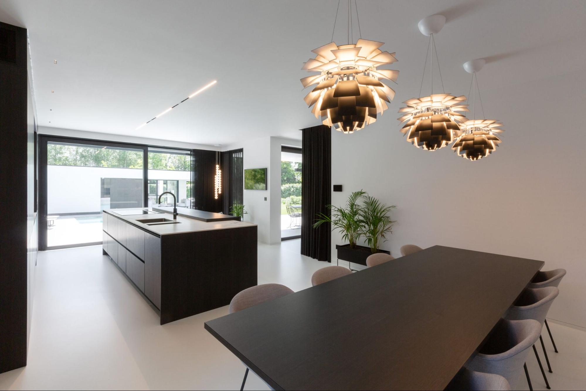 Moderne keuken met witte gietvloer, zwart keukeneiland en designverlichting boven de eettafel.<br />
