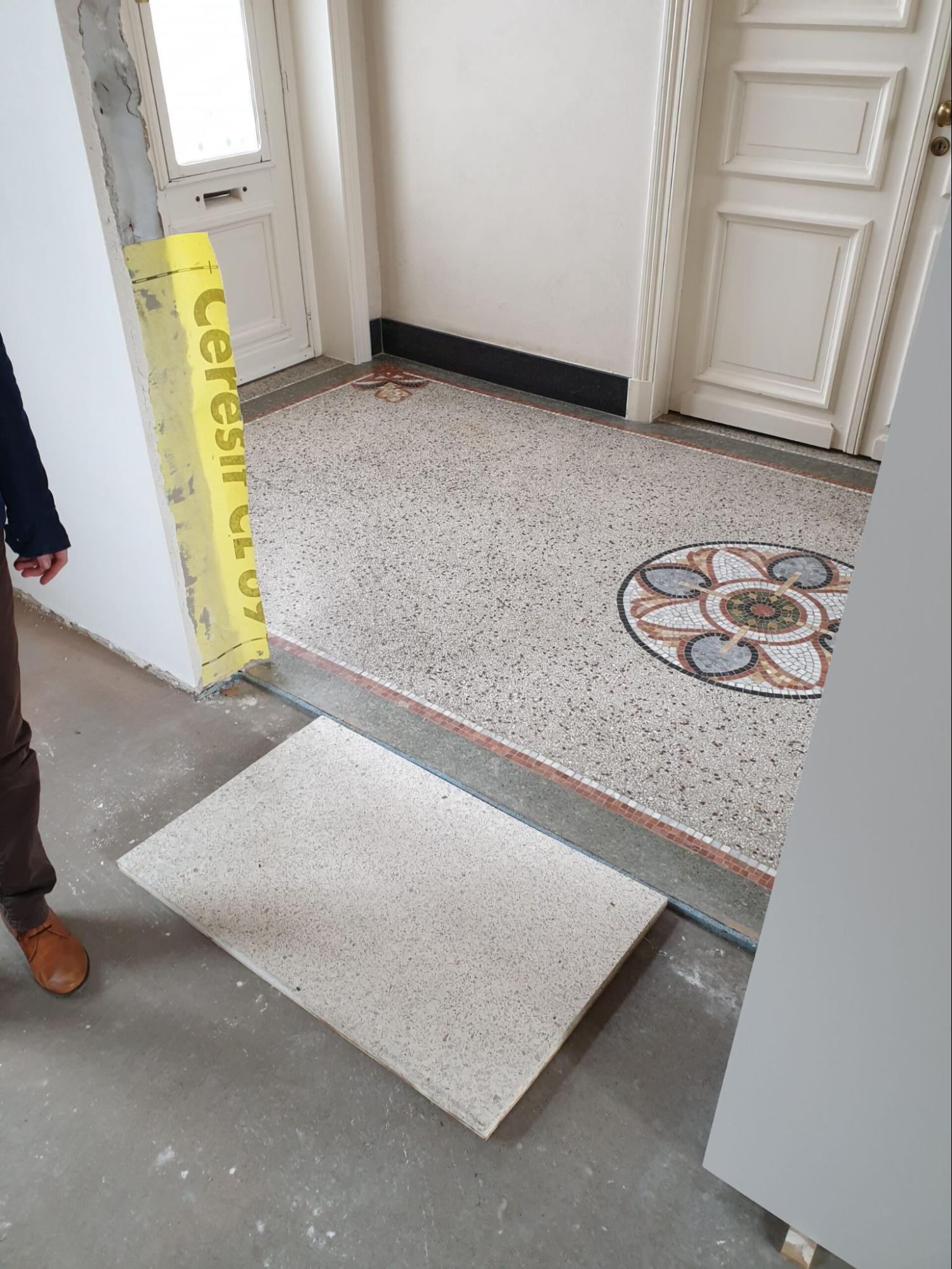Renovatie van authentieke terrazzo vloer in inkomhal met decoratief mozaïekmotief.