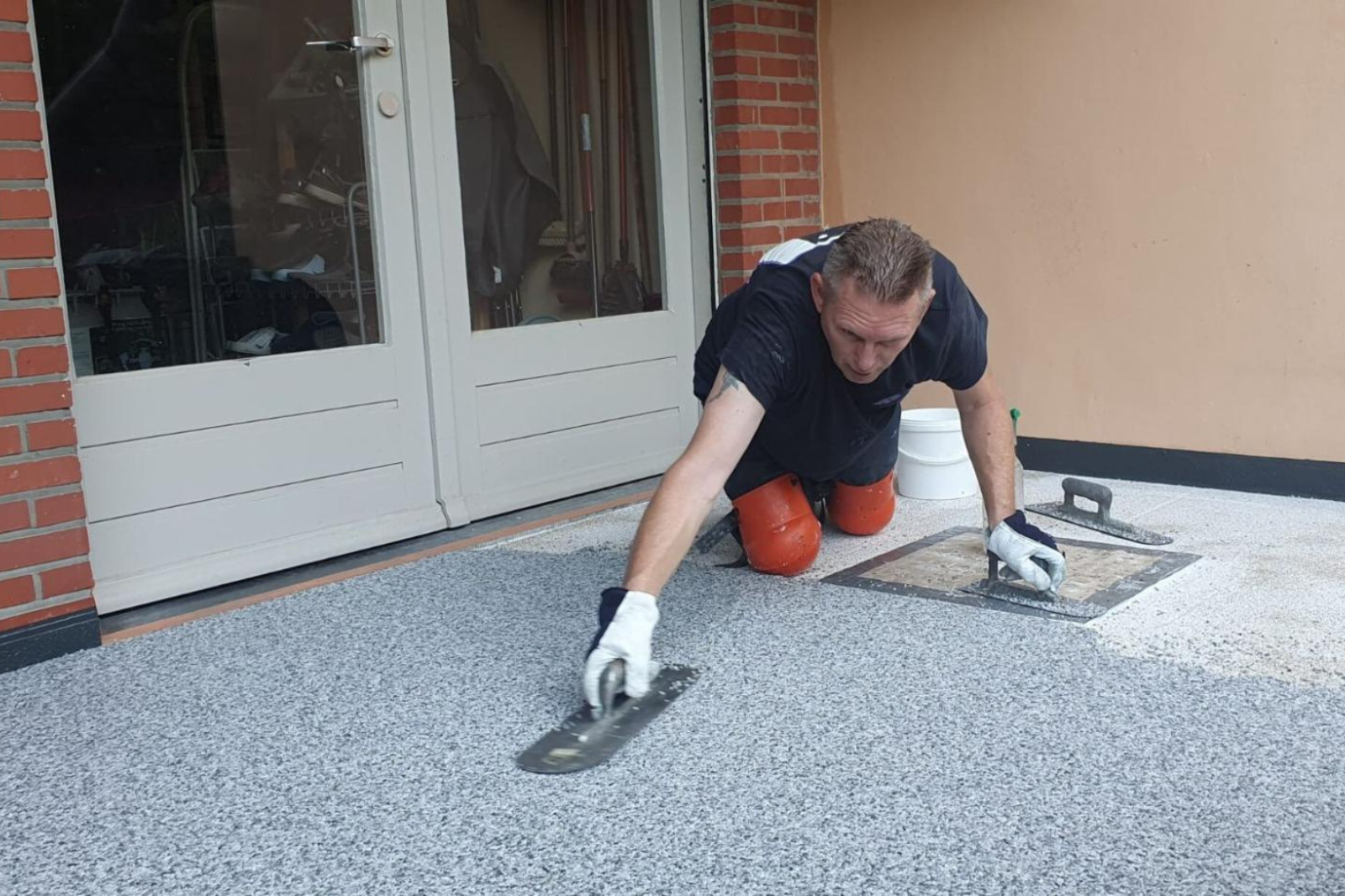 Plaatsing van marmertapijt op een terras waarbij een vakman de vloer handmatig afwerkt.