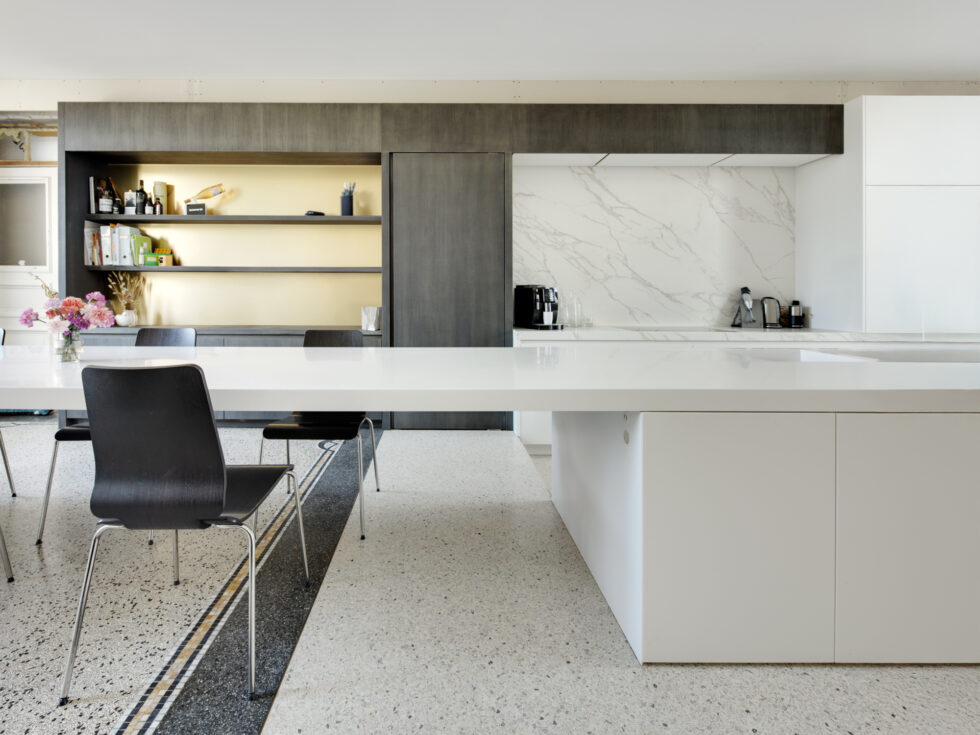 Terrazzo gietvloer in een moderne keuken met wit eiland en donkere houten kasten<br />
